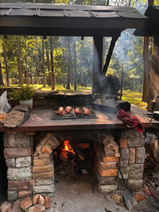 Wood-fired outdoor brick oven with smoke rising over meats on the grill